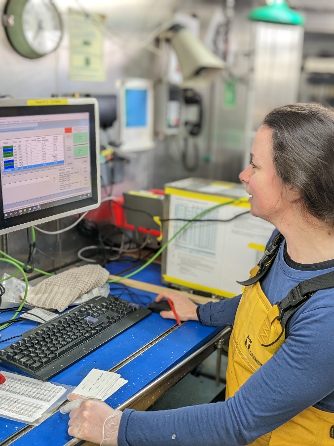 Survey team member in waterproof workwear reviewing sampling data on a computer in the vessel’s wet laboratory.